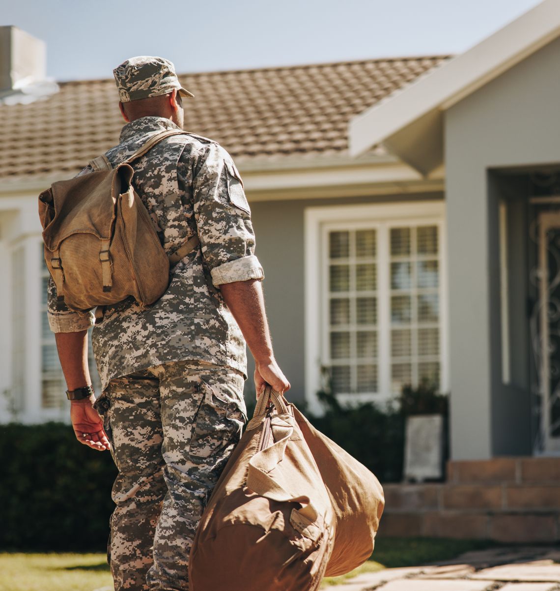 Patriotic young soldier walking towards his house with his luggage. Rearview of an American serviceman coming back home after serving in the military.